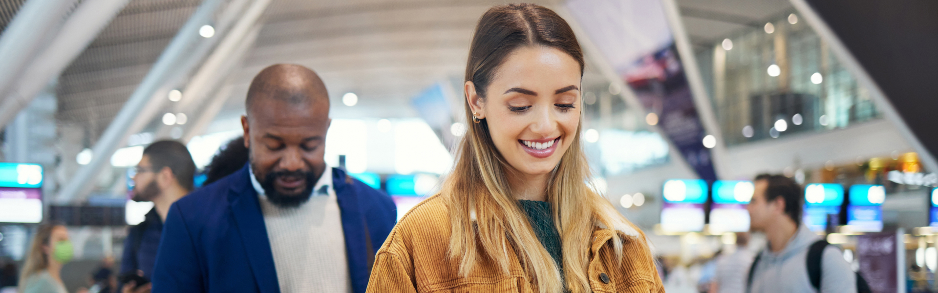 Grupo de pessoas caminhando no aeroporto carregando malas de rodinhas, com roupas coloridas