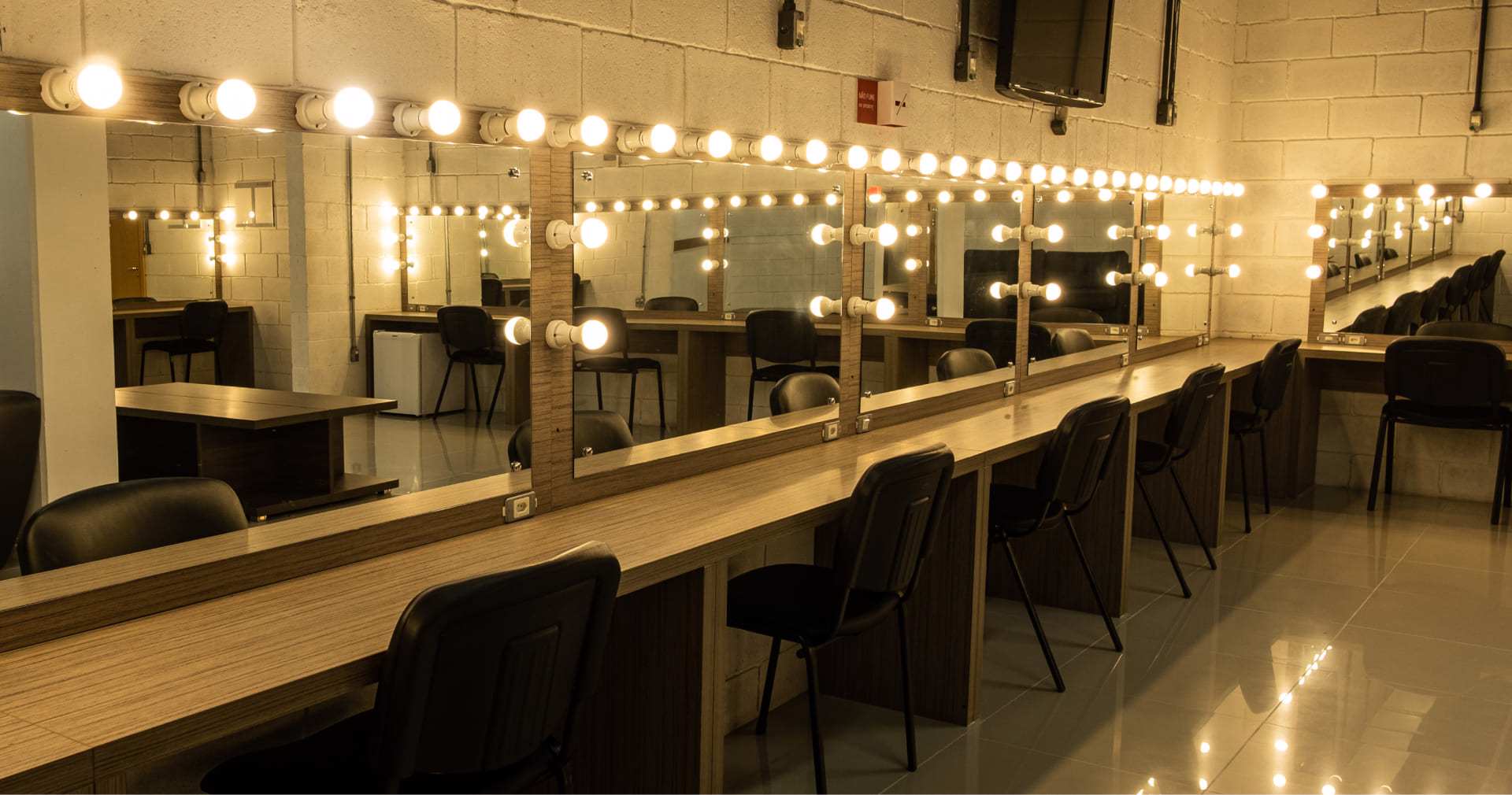 Camarim do Teatro, com uma bancada e cadeiras posicionadas em frente ao espelhos fixados na parede